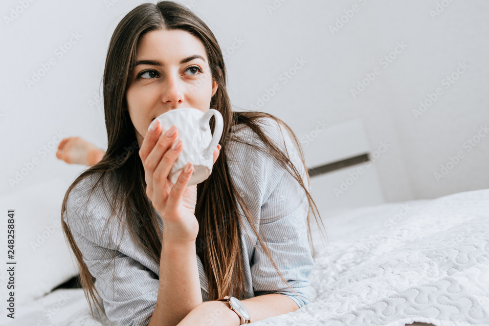 Young smiling woman drink a coffee in her bedroom. Happy morning.