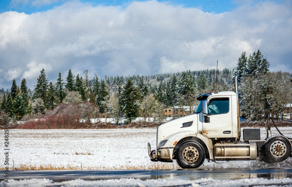 Profile of big rig semi truck with day cab for local delivery driving on the winter snowy road Profile of big rig semi truck with day cab for local delivery driving on the winter snowy road