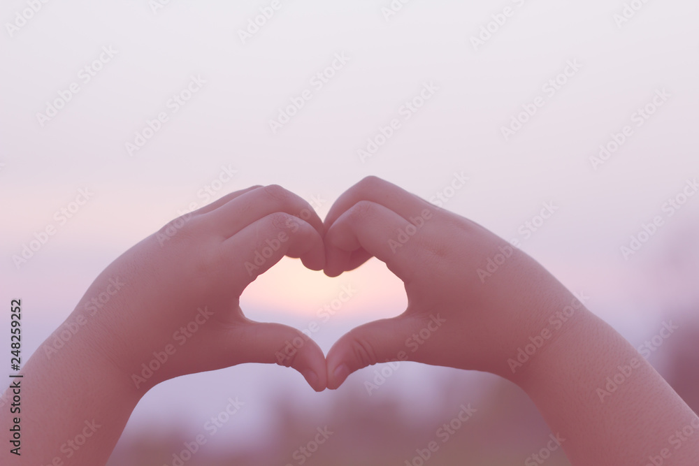 Fototapeta premium The silhouette of a kids hand in a beautiful sunrise captures the sun in the heart.