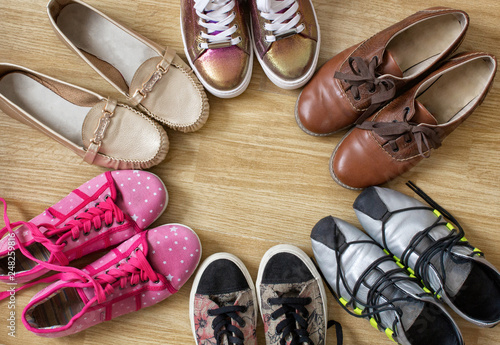 Various women's shoes and sneakers stand in the form of a circle with a free space in the middle, on a wooden background.