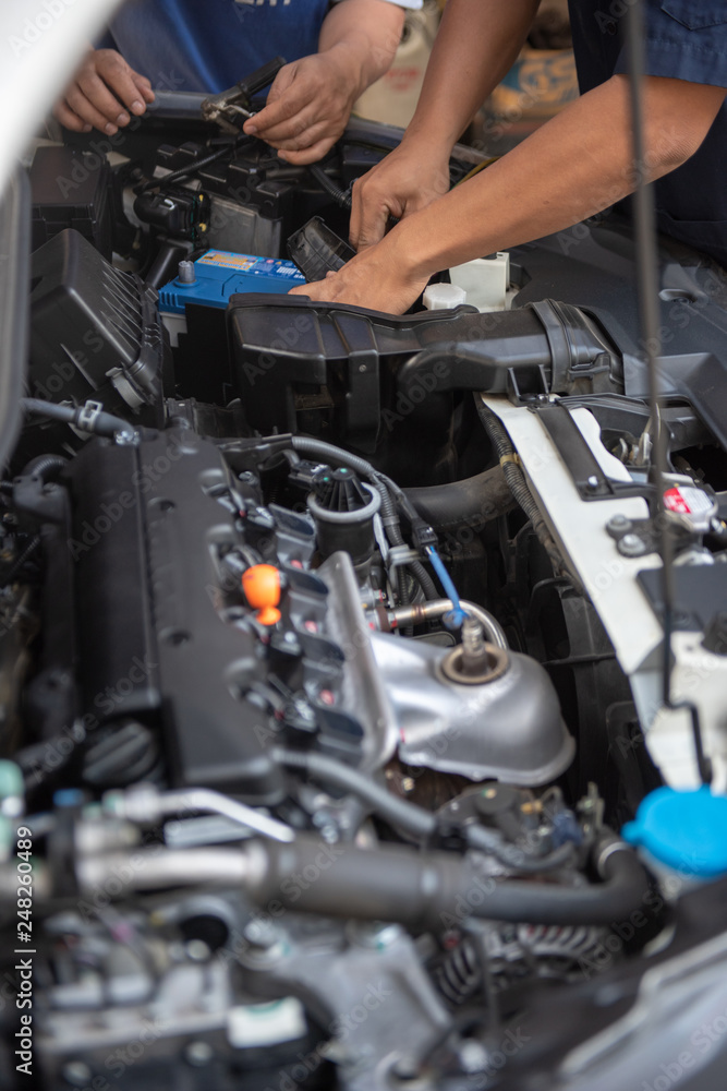 Car service by an auto mechanic in garage, fixing a car battery with wrench, also checking some parts of the engine showing by selective focus. Car service by an auto mechanic in garage, fixing a car battery with wrench, also checking some parts of the engine showing by selective focus.