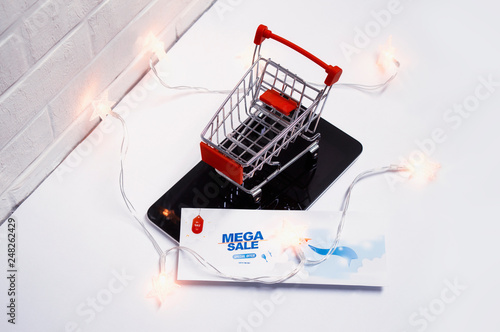 Online sale concept. Shopping cart and flyer with glowing lights on the tablet and on the background of a brick wall.