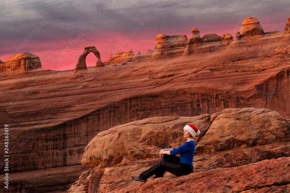 Woman sitting at viewpoint of Delicate Arch at sunrise. Christmas time in Utah. Moab. USA