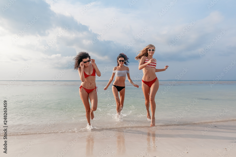 Three beautiful slender happy girlfriends having fun on the beach rejoicing and having fun against the background of the sea, vacation time and travel