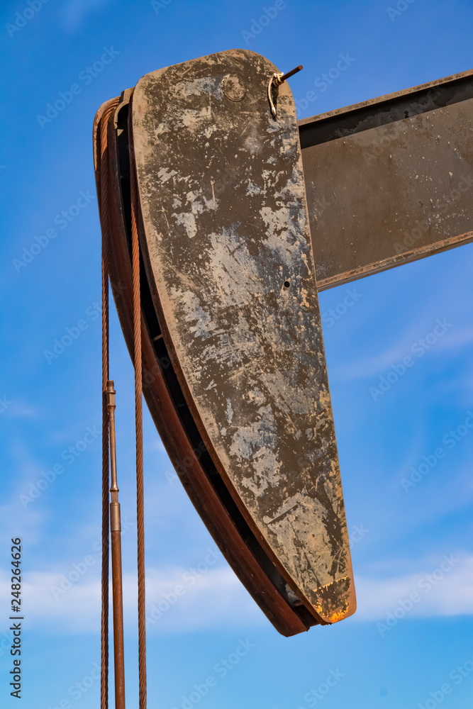 Head of old oil well grungy and close-up with rope against a blue sky with clouds.