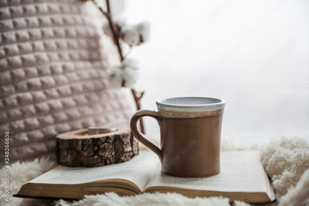 Details of still life in the home interior. Beautiful tea Cup, cut wood, book and pillows, cotton flower on a windowsill. Vintage, rustic. Cosy autumn-winter concept. Copy space Details of still life in the home interior. Beautiful tea Cup, cut wood, book and pillows, cotton flower on a windowsill. Vintage, rustic. Cosy autumn-winter concept. Copy space