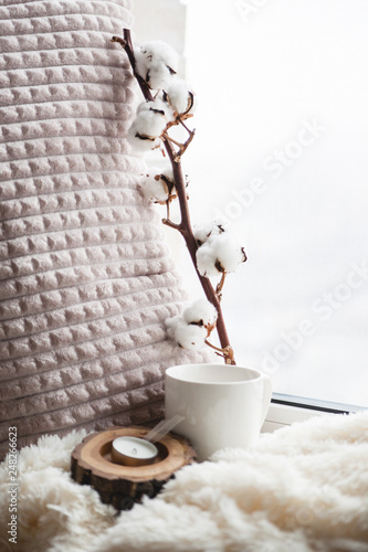 Details of still life in the home interior. Beautiful tea Cup, cut wood, book and pillows, cotton flower on a windowsill. Vintage, rustic. Cosy autumn-winter concept. Copy space