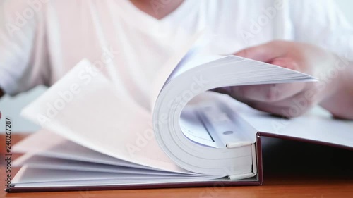Slow motion of a man is opening large books to find information by trying to open many pages quickly on the table.