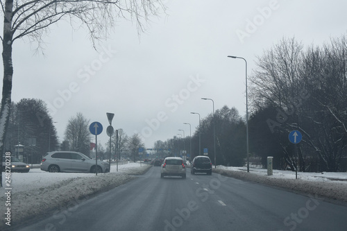 City street traffic cars drive on snow covered cityscape in grey overcast weather winter.