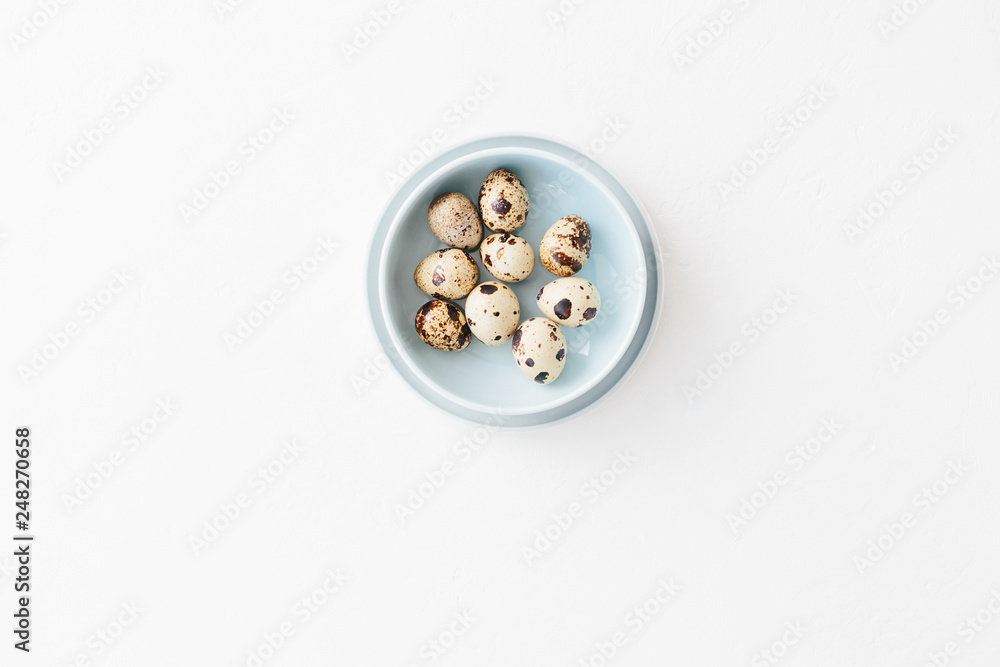 Quail eggs in light blue bowl on white textured background Quail eggs in light blue bowl on white textured background