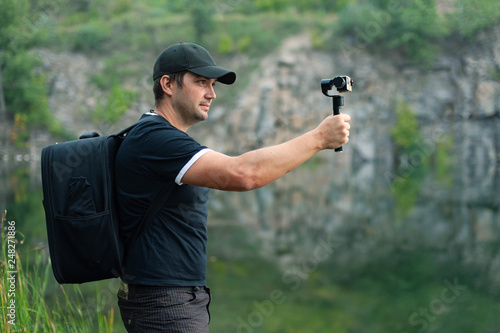 Male tourist with backpack shooting video on action camera in nature
