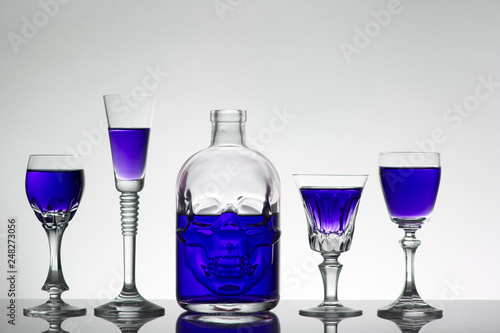 A skull bottle and crystal glasses with a liquid, alcohol drink.