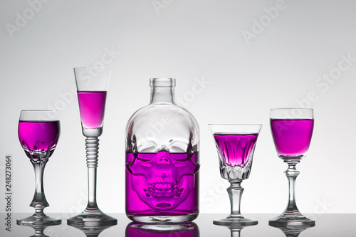 A skull bottle and crystal glasses with a liquid, alcohol drink.