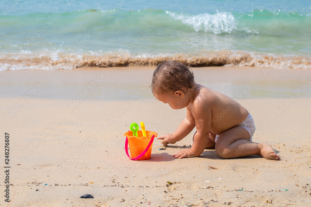 Happy child playing in summer on the blue sea. Baby crawls on the beach and plays with toys Happy child playing in summer on the blue sea. Baby crawls on the beach and plays with toys
