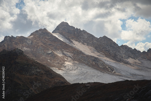 Mountain landscape dusty dirty volcanic slope with a cracked melting glacier against the backdrop of the Caucasus Mountains. Global warming. Glaciers of the North Caucasus