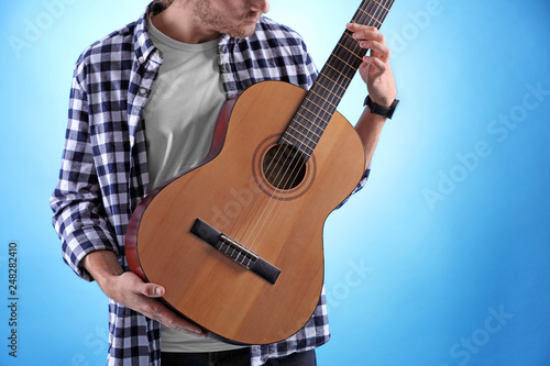 Young man playing acoustic guitar on color background, closeup