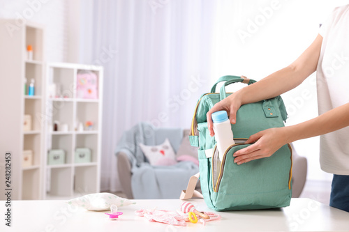 Woman packing baby accessories into maternity backpack on table indoors, closeup. Space for text