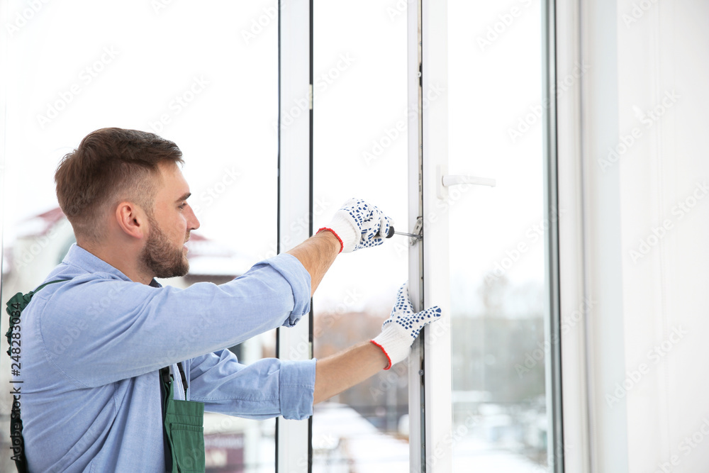 Fototapeta premium Construction worker adjusting installed window with screwdriver indoors