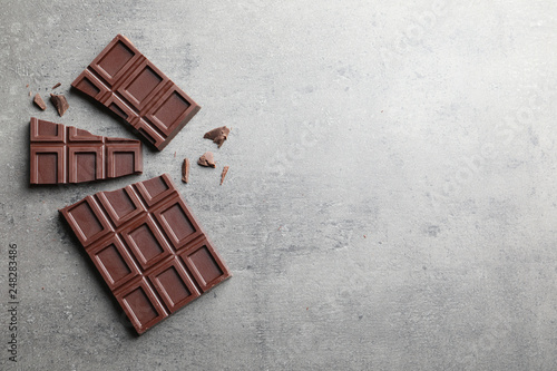 Pieces of tasty chocolate on grey background, flat lay. Space for text