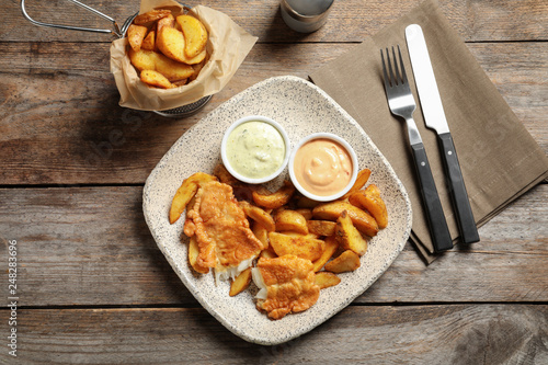 Plate with British traditional fish and potato chips on wooden background, top view