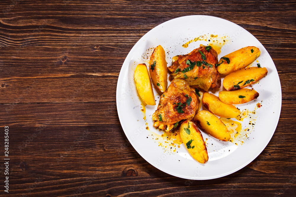 Grilled chicken thighs with baked potatoes on wooden table Grilled chicken thighs with baked potatoes on wooden table