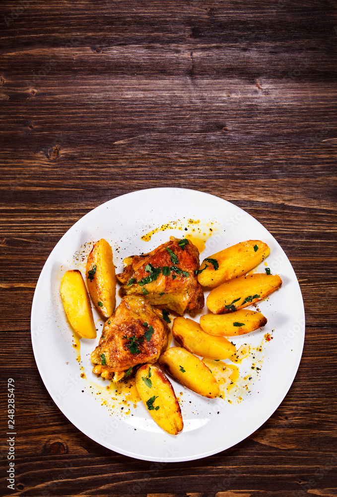 Grilled chicken thighs with baked potatoes on wooden table Grilled chicken thighs with baked potatoes on wooden table