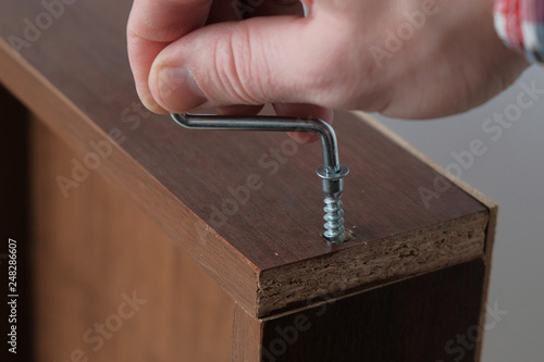Process of assembling a furniture drawer, hand tightens  screw, close-up.
