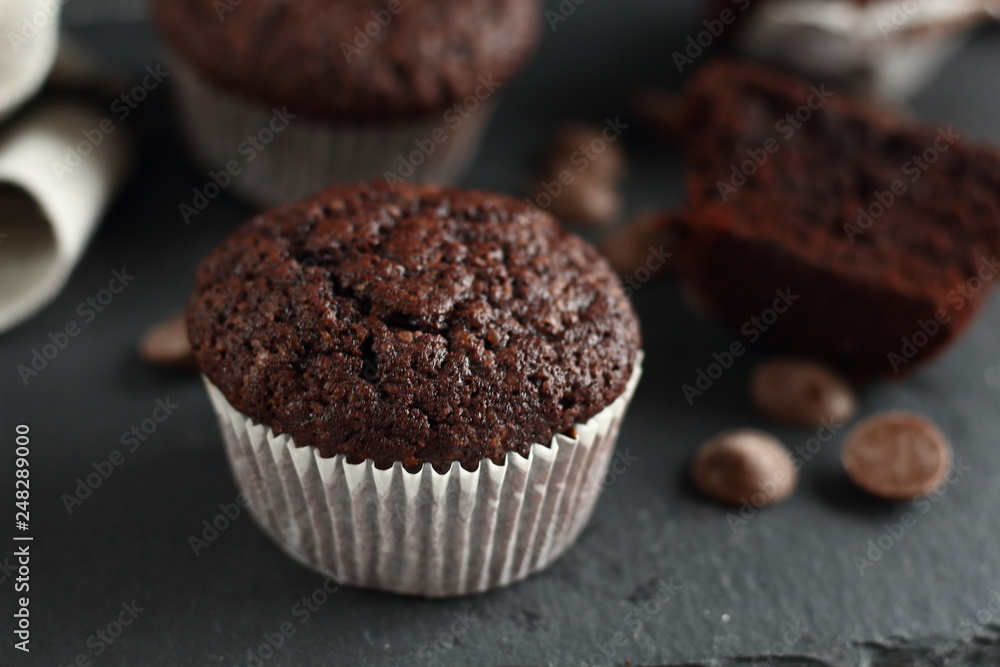 Chocolate homemade cupcakes muffins on a black background with chocolate drops in the background. Bakery style. Dark food photo Chocolate homemade cupcakes muffins on a black background with chocolate drops in the background. Bakery style. Dark food photo