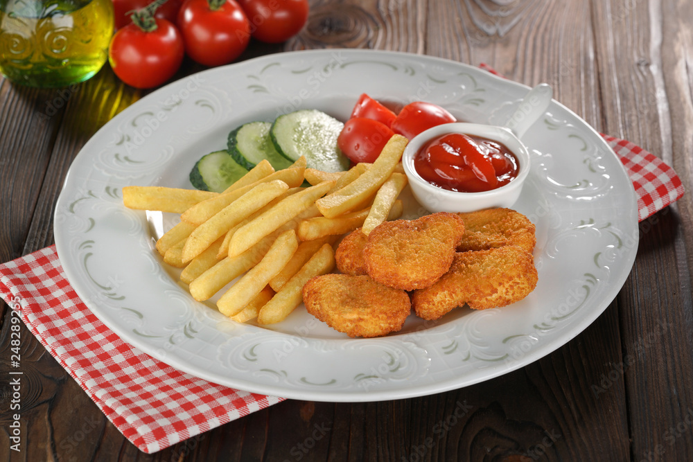 Chicken nuggets, french fries and vegetables in white plate on wooden table Chicken nuggets, french fries and vegetables in white plate on wooden table