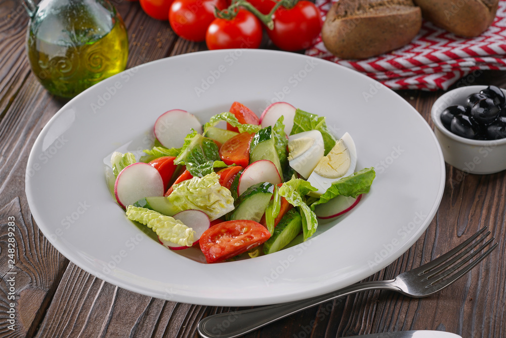 Vegetable salad with eggs, tomatoes and lettuce served in white plate on wooden background