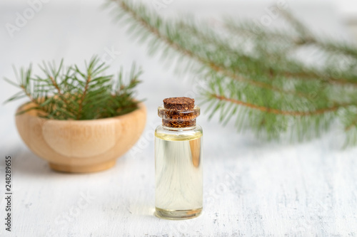 Pine essential oil in a glass bottle. Soft focus. White wooden background.