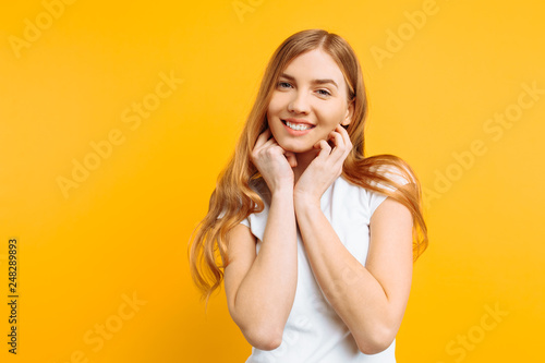 beautiful girl in white t-shirt holding hands near face, portrait of cute woman on yellow background
