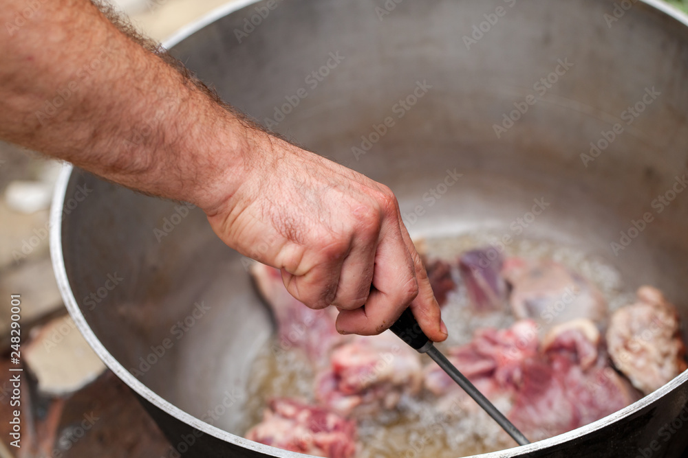 Fototapeta premium Cook mixes lamb pieces in cauldron