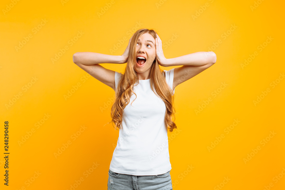 Portrait of an annoyed woman covering her ears and screaming from a terrible noise, on a yellow background Portrait of an annoyed woman covering her ears and screaming from a terrible noise, on a yellow background