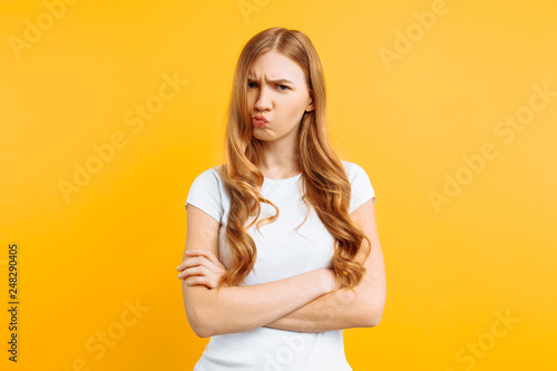Fototapeta Portrait of an upset young girl standing with folded arms and offended face, on