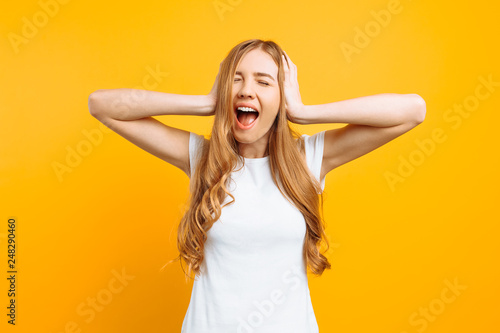 Portrait of an annoyed woman covering her ears and screaming from a terrible noise, on a yellow background