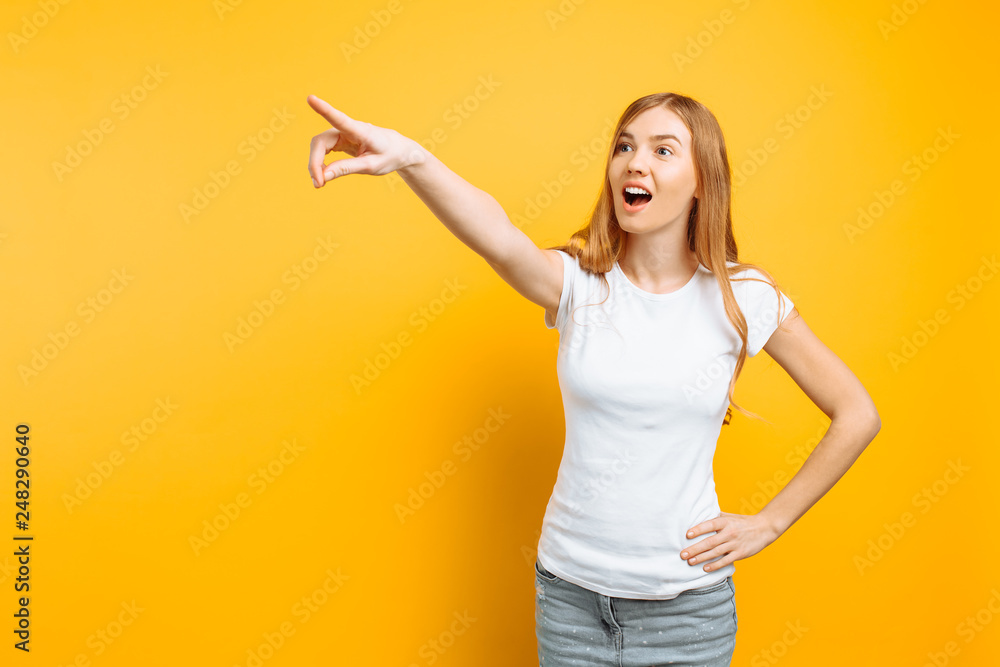 girl looking into the distance, pointing with index finger to something isolated on yellow background. girl looking into the distance, pointing with index finger to something isolated on yellow background.