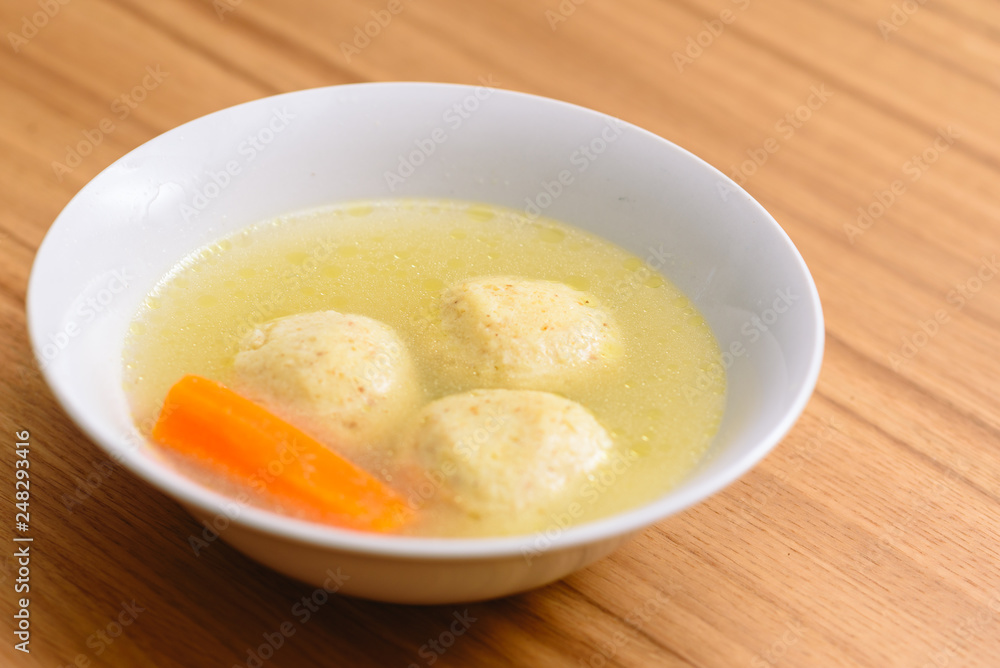 Traditional matzoh ball (kneidlach) soup.White bowl with authentic matzo ball chicken taste hot soup ( bouillon ) tradition Jewish food for Passover and every day. Traditional matzoh ball (kneidlach) soup.White bowl with authentic matzo ball chicken taste hot soup ( bouillon ) tradition Jewish food for Passover and every day.