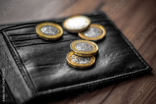 New Great British Pound GBP Coins laying casually on top of black wallet on wooden surface. Wealth, Money, Cash, Change.
