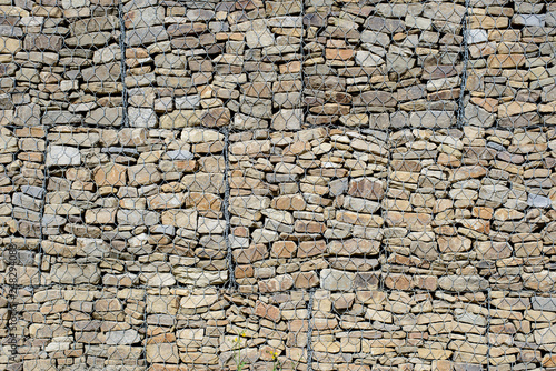 the wall of beautiful multi-colored stones covered with iron mesh