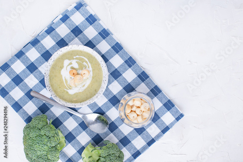 Cream soup puree with broccoli, cream and crackers. Lunch of vegetables on a light background. Plate and napkin on the table.