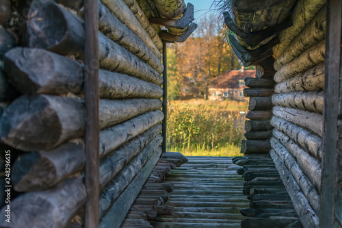 View to the small house in autumn forest through the narrow lane between two old log huts of ancient Lake Castle in Araisi Archaeological Museum Park, Latvia. photo