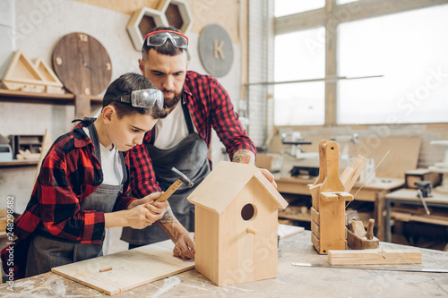 Obraz na plátne Carpenter building a wooden birdhouse together with his kid
