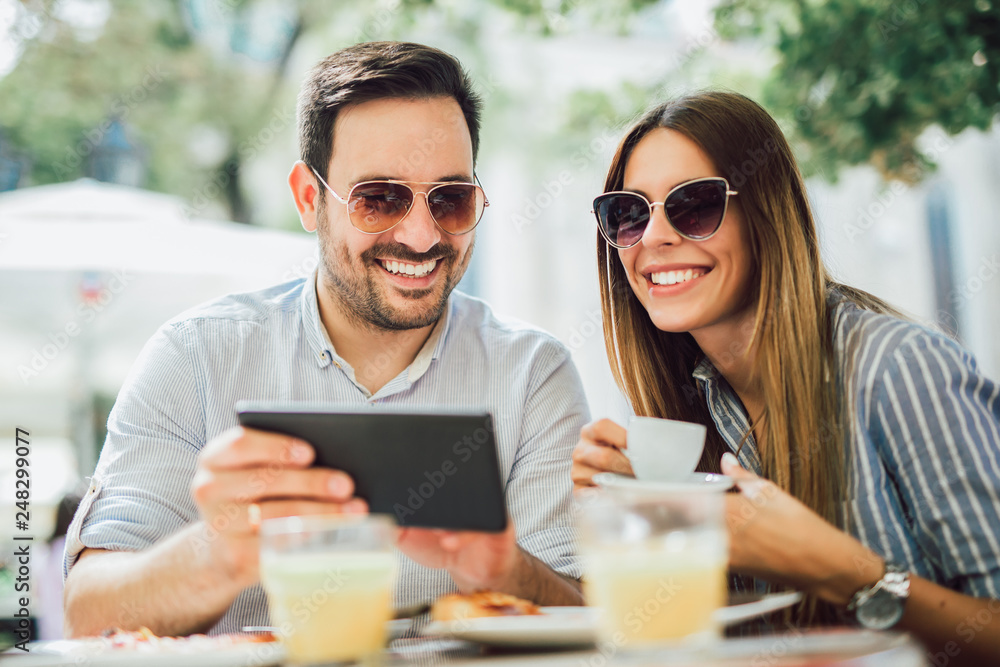 Cute couple looking at a tablet at the cafe terrace Cute couple looking at a tablet at the cafe terrace