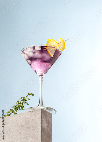 Cold cocktail with lavender syrup and lemon with ice on a light blue background.