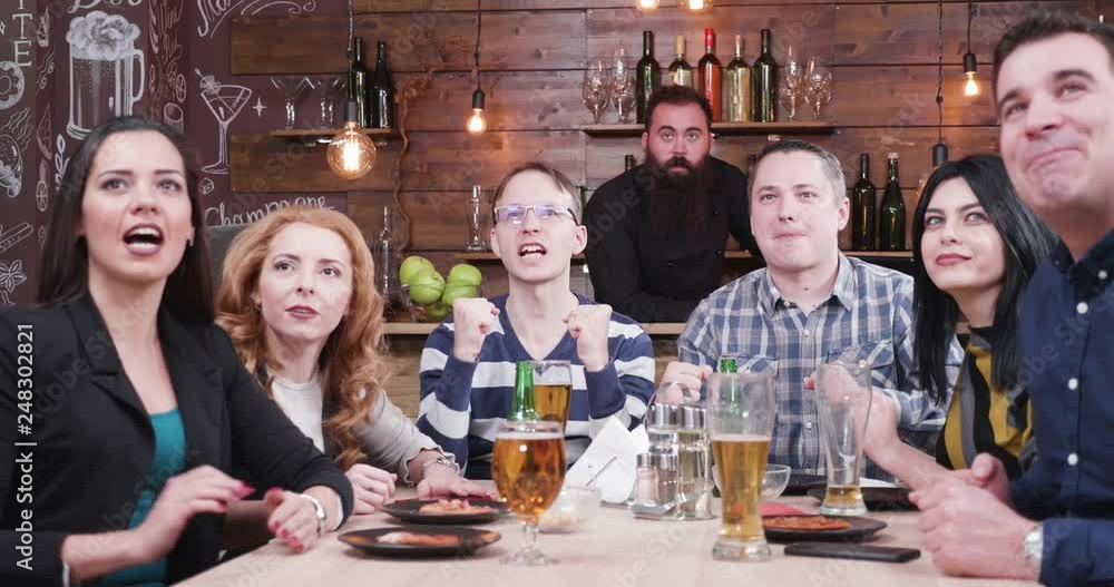 Group of friends watch a sport game on a TV in a vintage pub or restaurant. They all cheer and are happy when the team scores Group of friends watch a sport game on a TV in a vintage pub or restaurant. They all cheer and are happy when the team scores