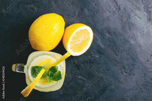 Refreshing lemonade drink with lemon slice and mint in the jar on dark background, top view