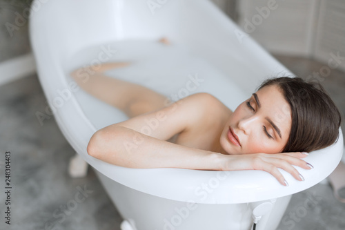 Attractive young woman with healthy white skin and brown hair  chilling in spa salon  taking milk bath with eyes  closed in enjoyment