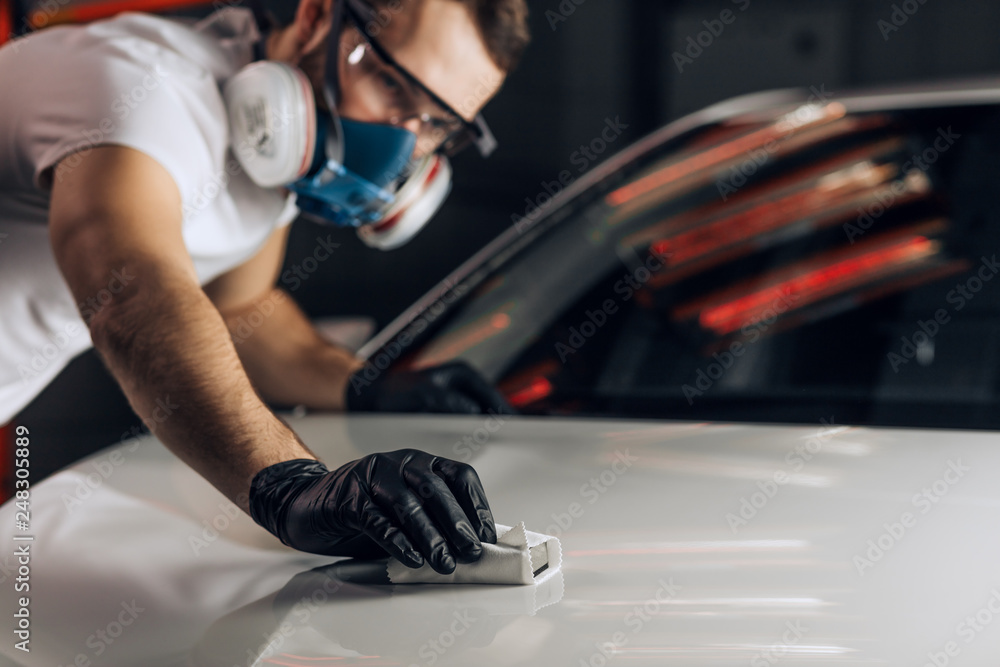 © alfa27 - young man clears polish a vehicle. close up photo. copy space. mecchanic using sandpaper at workplace