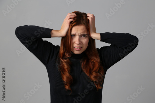 The redhead girl has a terrible headhache migraine at gray background photo